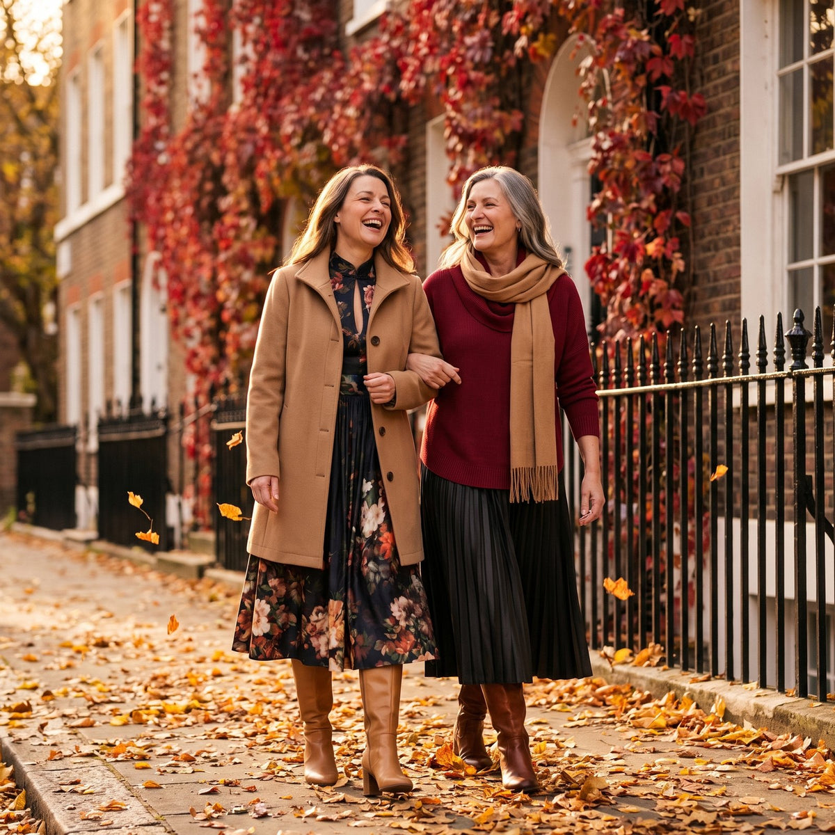 Two friends in autumn coats and a floral dress walking through fallen leaves in London